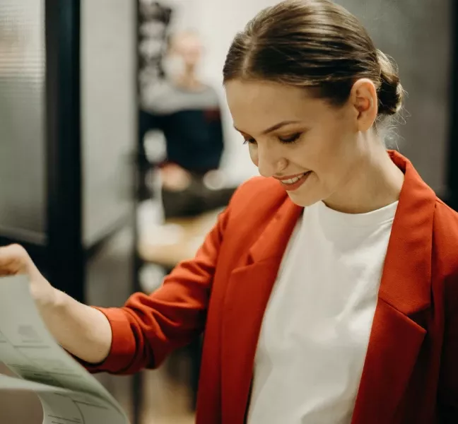 Person i röd kavaj ler medan hon arbetar med dokument på kontor