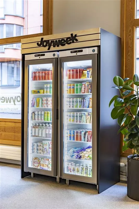 Kylskåp fyllt med drycker och snacks i ett kontor med Joyweek-logotyp ovanför