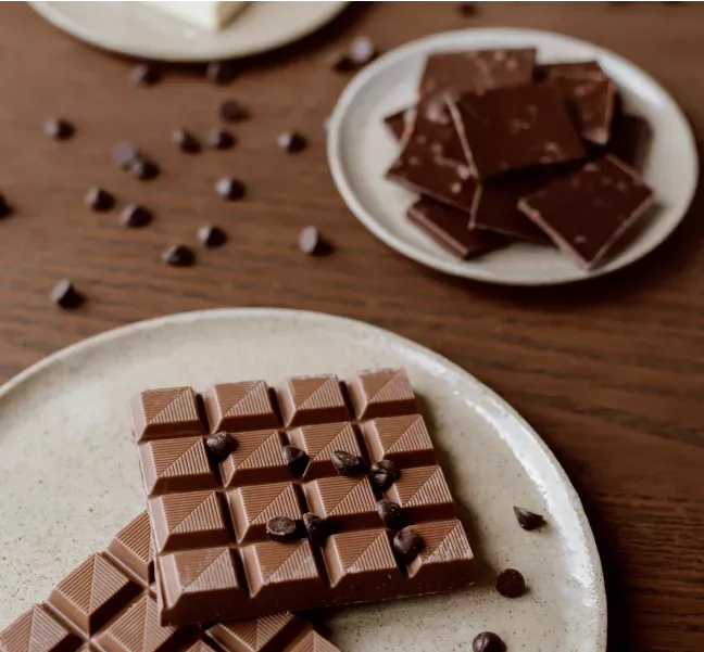 Tallrikar med chokladbitar och snacks på ett bord, symbol för fika och mat på arbetsplatsen